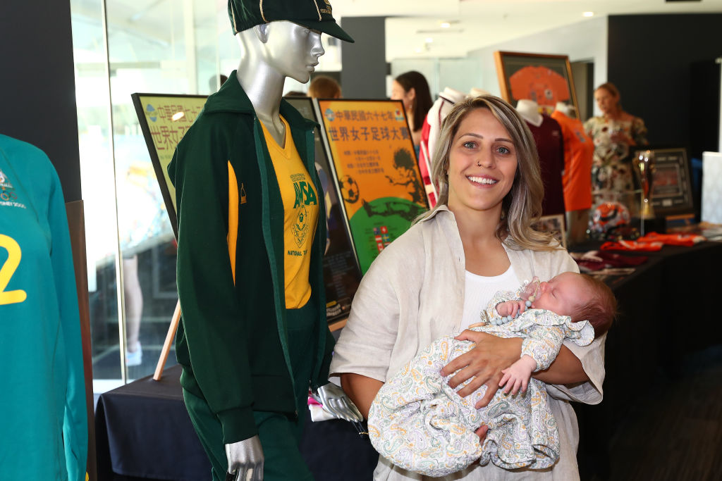 BRISBANE, AUSTRALIA - SEPTEMBER 24: Katrina Gorry and daughter Harper pose with memorabilia during the Australian Women's Football Centenary Event at The Gabba on September 24, 2021 in Brisbane, Australia. (Photo by Chris Hyde/Getty Images for Football Australia)